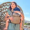 Mutter mit Kind in Babytrage Leolin Maxi Sand Melange am Meer