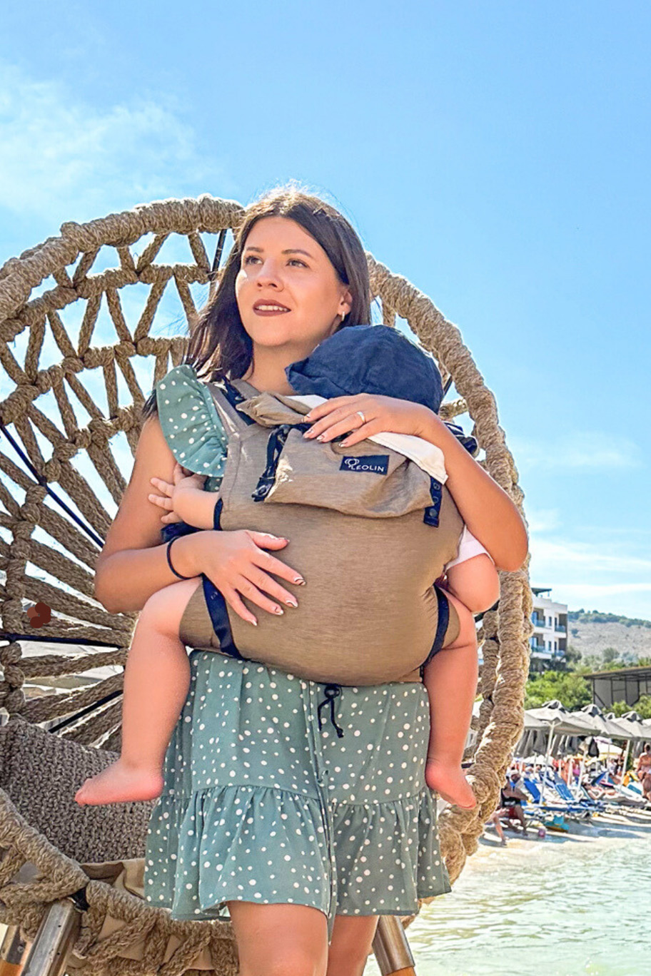 Mutter mit Kind in Babytrage Leolin Maxi Sand Melange am Meer